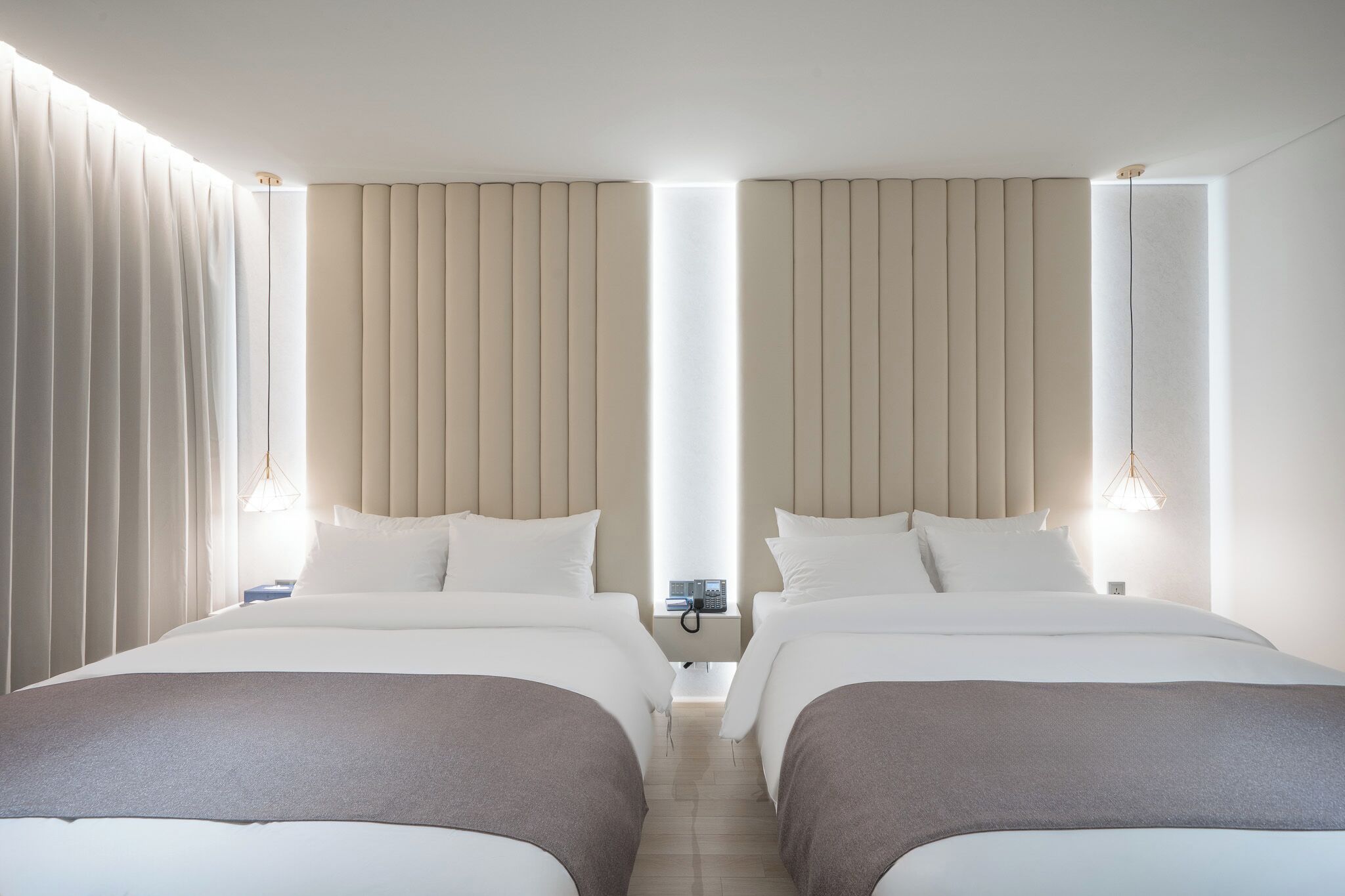 A hotel room with two beds, a bedside table with a phone, and a window with curtains.