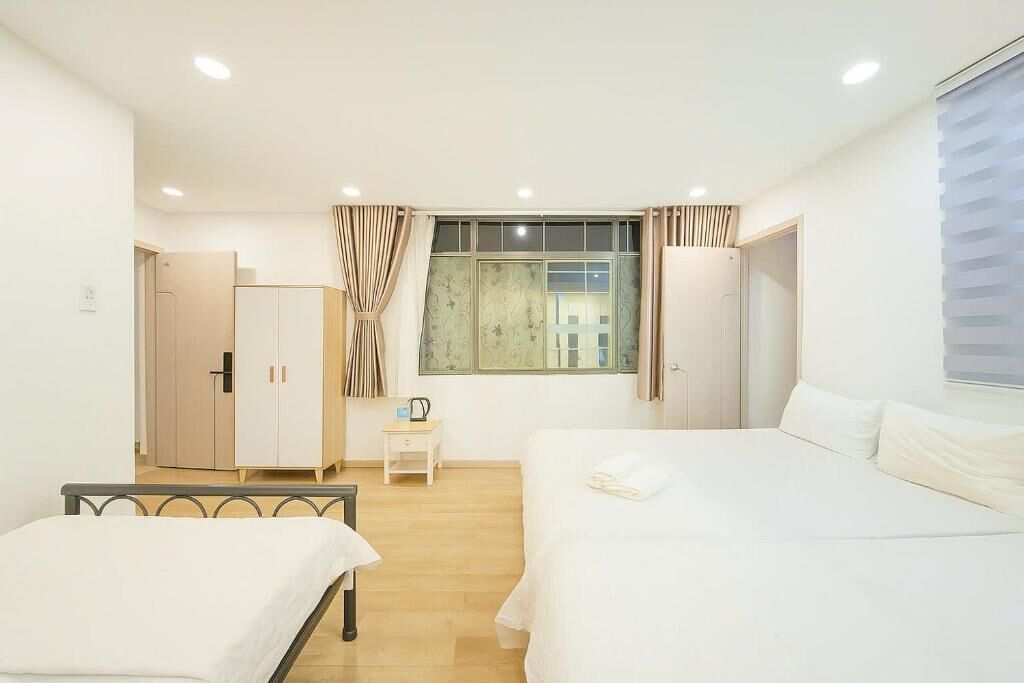 A bedroom with two beds, a wardrobe, a small table, and a window with curtains.