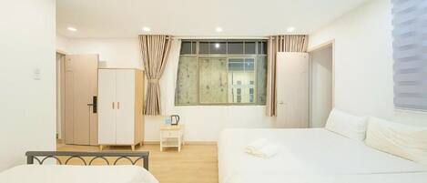 A bedroom with two beds, a wardrobe, a small table, and a window with curtains.