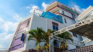 Un hotel de diseño moderno, con un letrero llamativo, varias ventanas y un área exterior cubierta con palmeras.