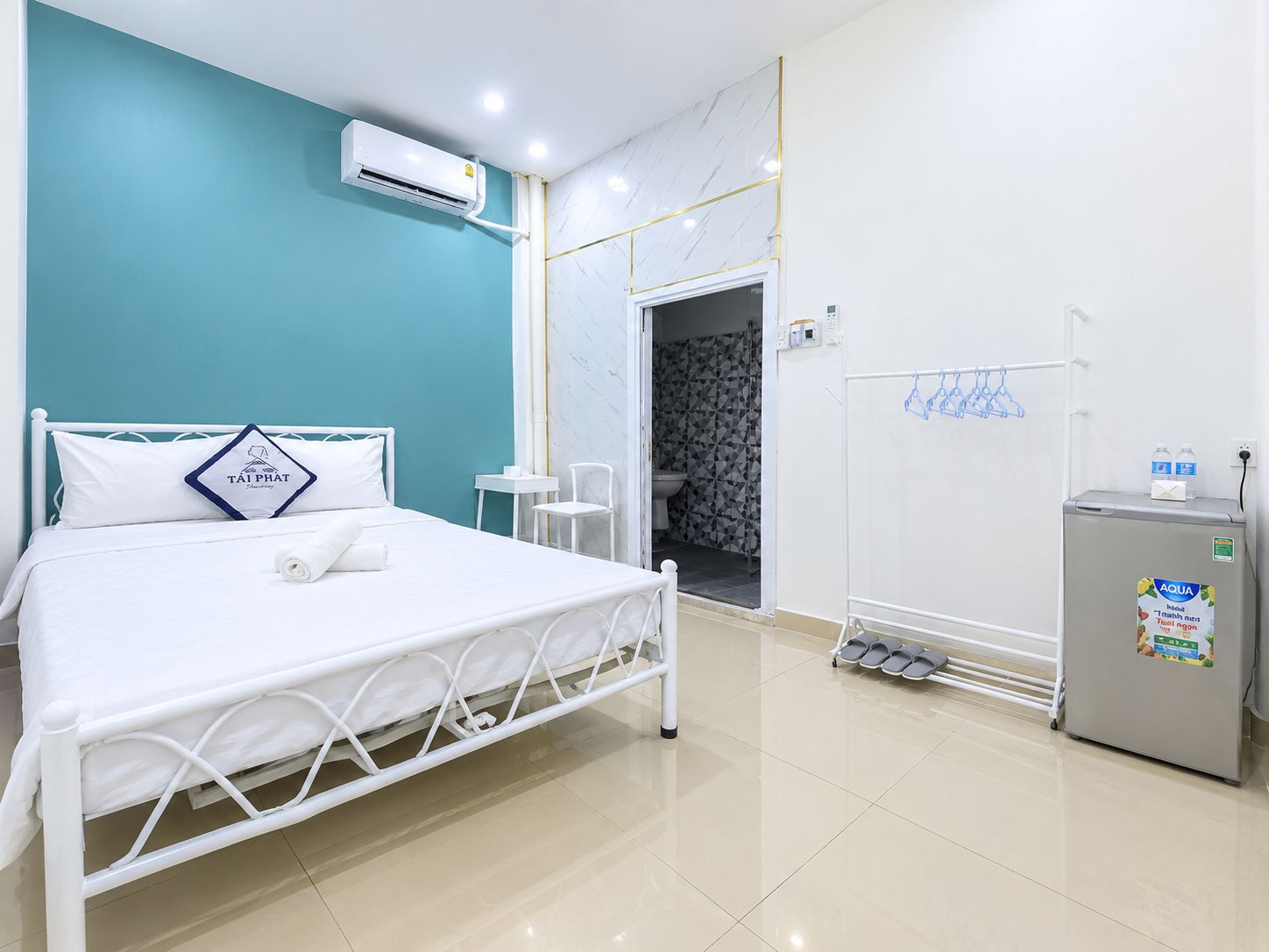 Une chambre d’hôtel équipée d’un lit, d’un appareil de climatisation, d’un réfrigérateur et d’une salle de bain, le tout visible à travers une porte ouverte.
