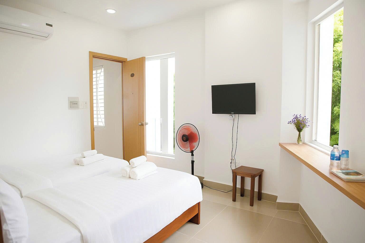 A hotel room with a bed, a TV, a fan, a small table, and a window with a view.