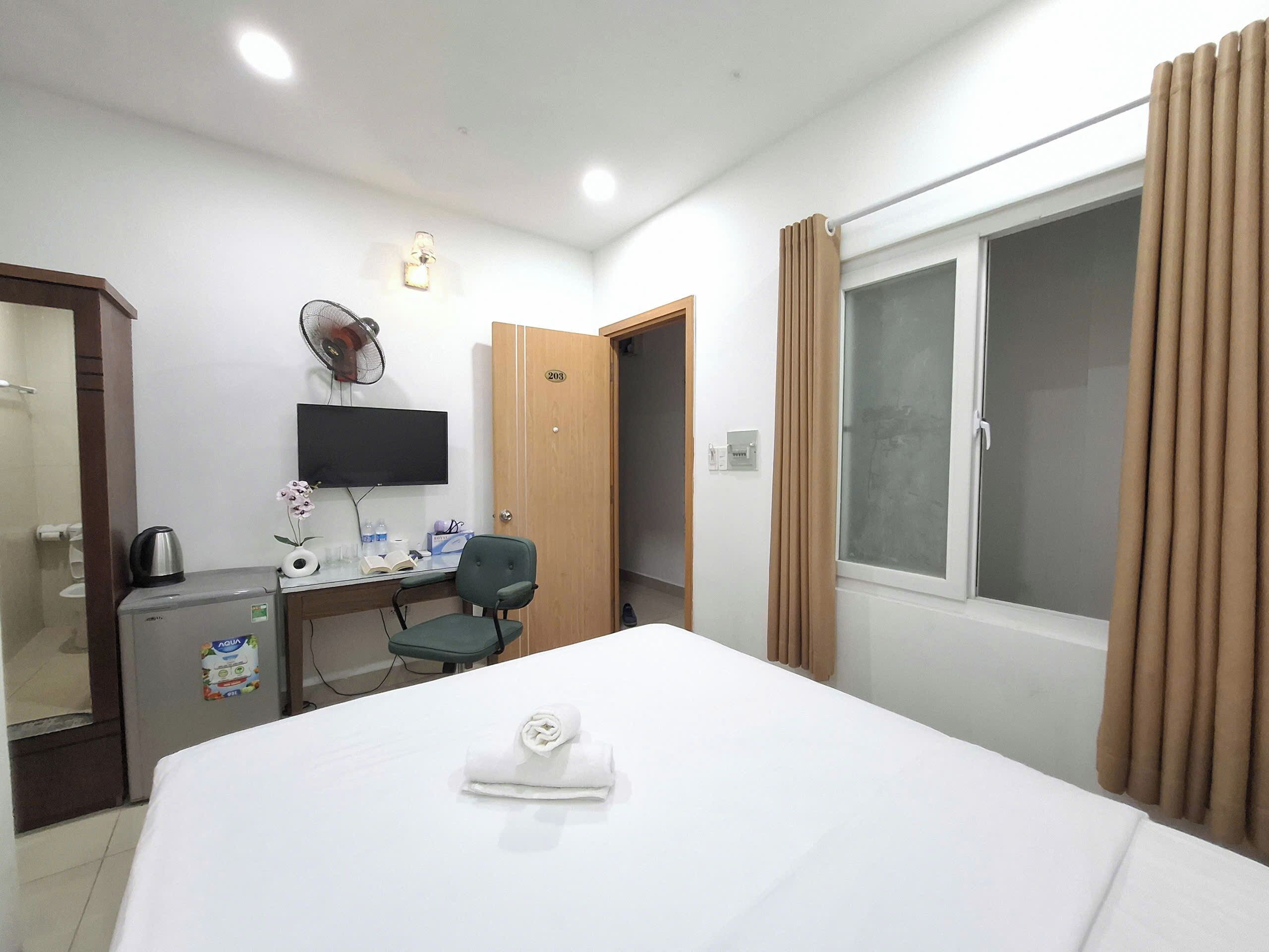 A hotel room with a bed, desk, chair, TV, and a window with curtains.