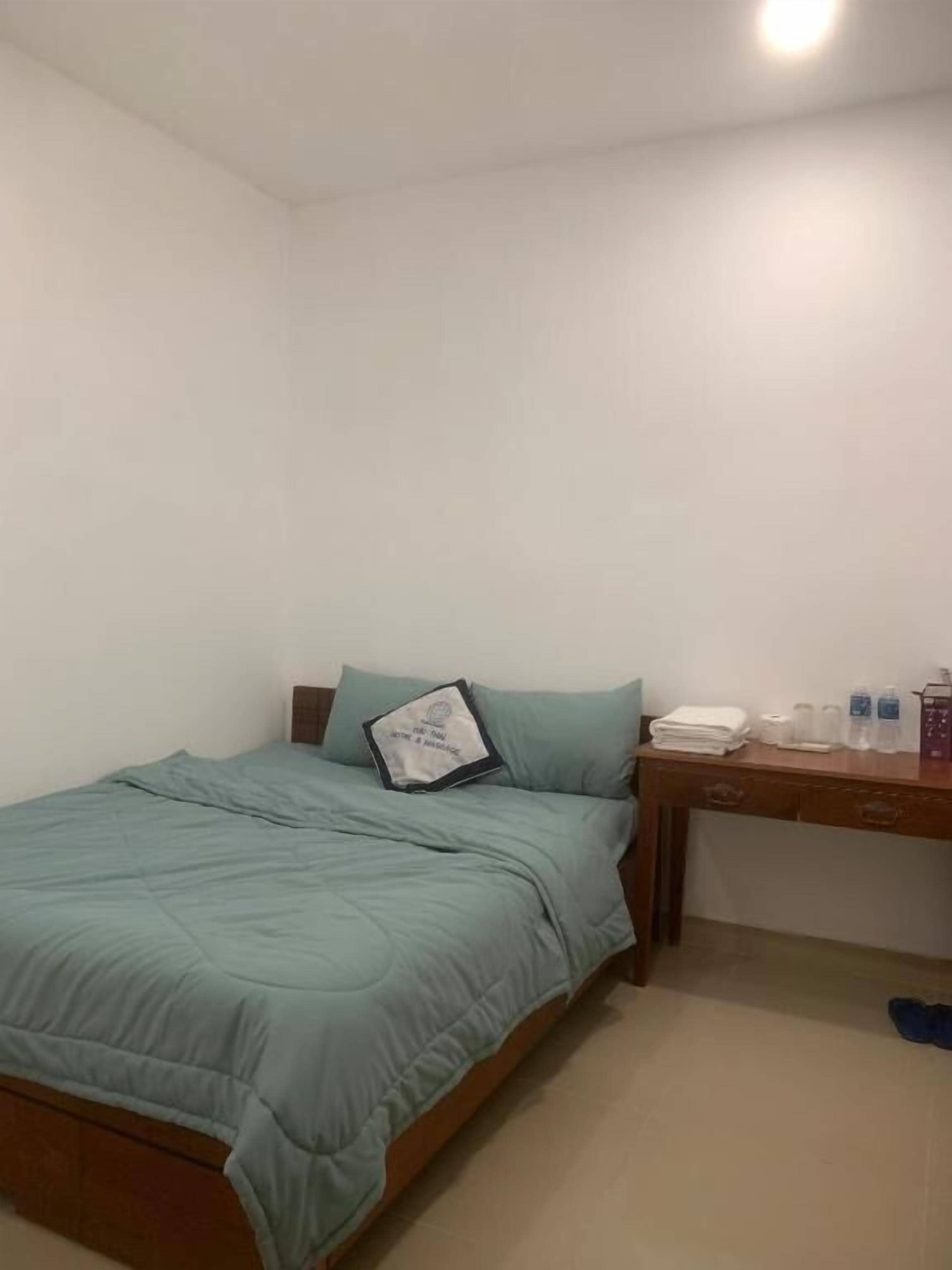 A bedroom with a bed, a desk, and a nightstand.
