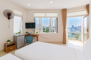A hotel room with a bed, desk, chair, TV, and a city view through large windows. - Lunaria Maison - Thu Thai Homestay (Ho Chi Minh City)