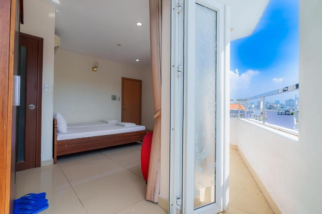 A balcony with a city view, a bed with a red pillow, and a door leading to another room.