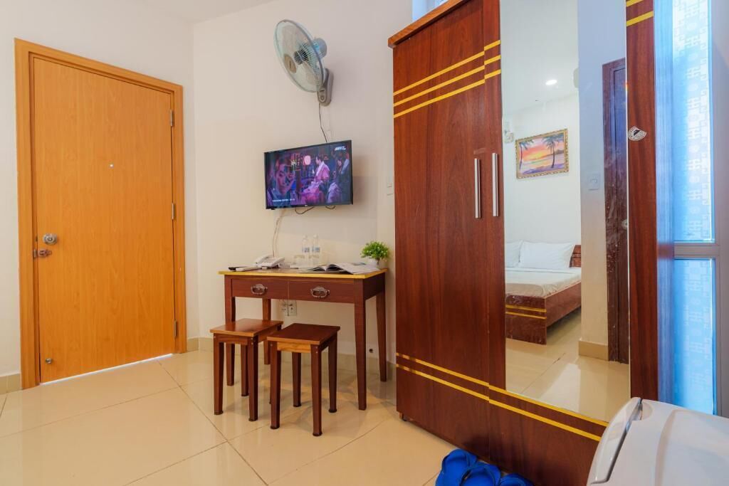 Une chambre d’hôtel avec une armoire en bois, un bureau avec deux chaises, une télévision et un lit avec une table de chevet.