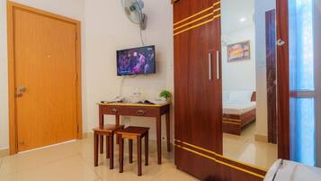 A hotel room with a wooden wardrobe, a desk with two chairs, a television, and a bed with a nightstand.