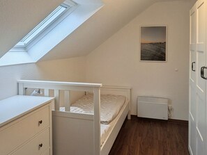 Ein Schlafzimmer mit schrägem Dach, einem Bett, einem Heizkörper, einem Kleiderschrank und einem Bild an der Wand.