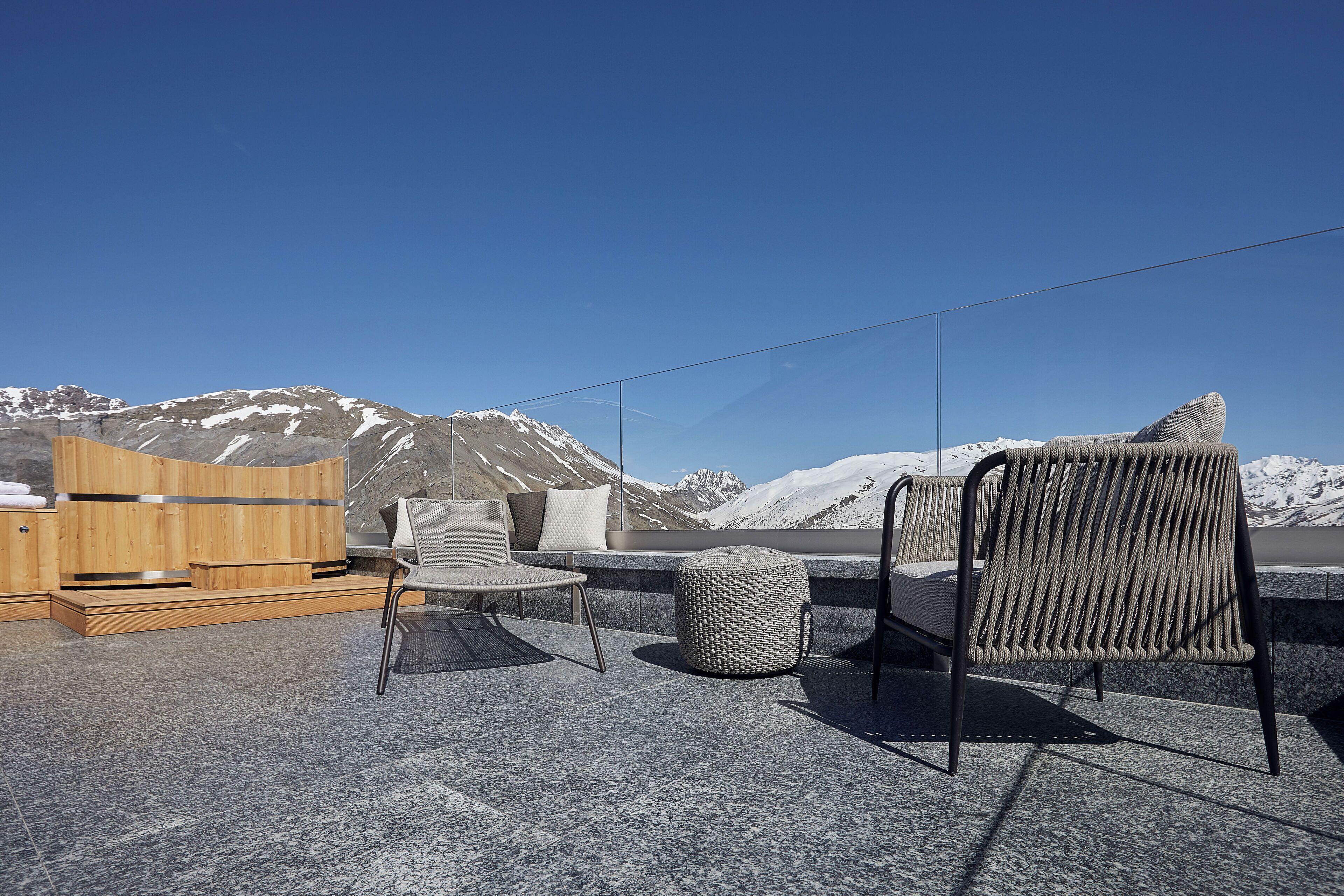Une terrasse dotée d’un sauna en bois, d’un fauteuil rembourré, d’un pouf en osier et d’une chaise à armature métallique avec un dossier en osier.