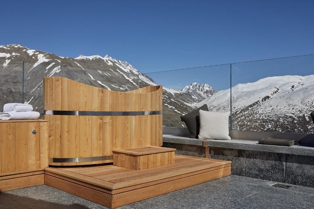 Una sauna de madera con un banco de piedra y vistas a montañas nevadas.