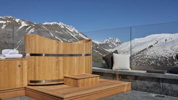 Una sauna de madera con un banco de piedra y vistas a montañas nevadas.