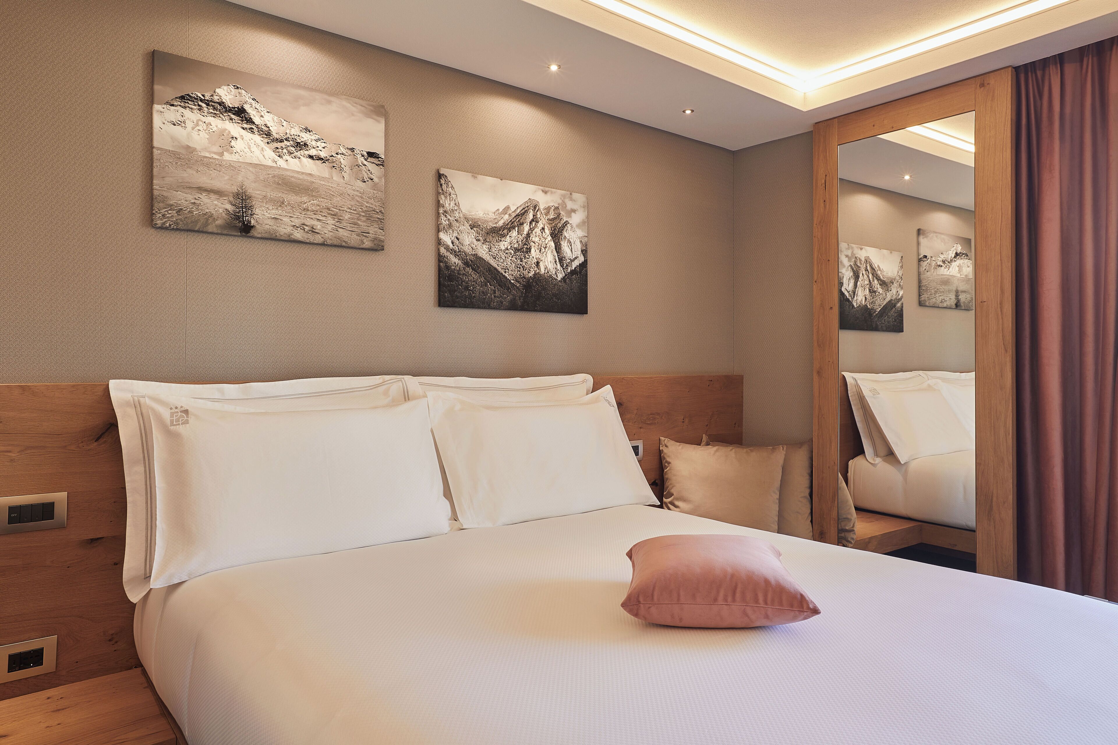 A hotel room with a large bed, wooden headboard, and two mountain landscape paintings on the wall.