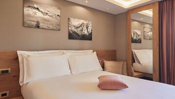 A hotel room with a large bed, wooden headboard, and two mountain landscape paintings on the wall.