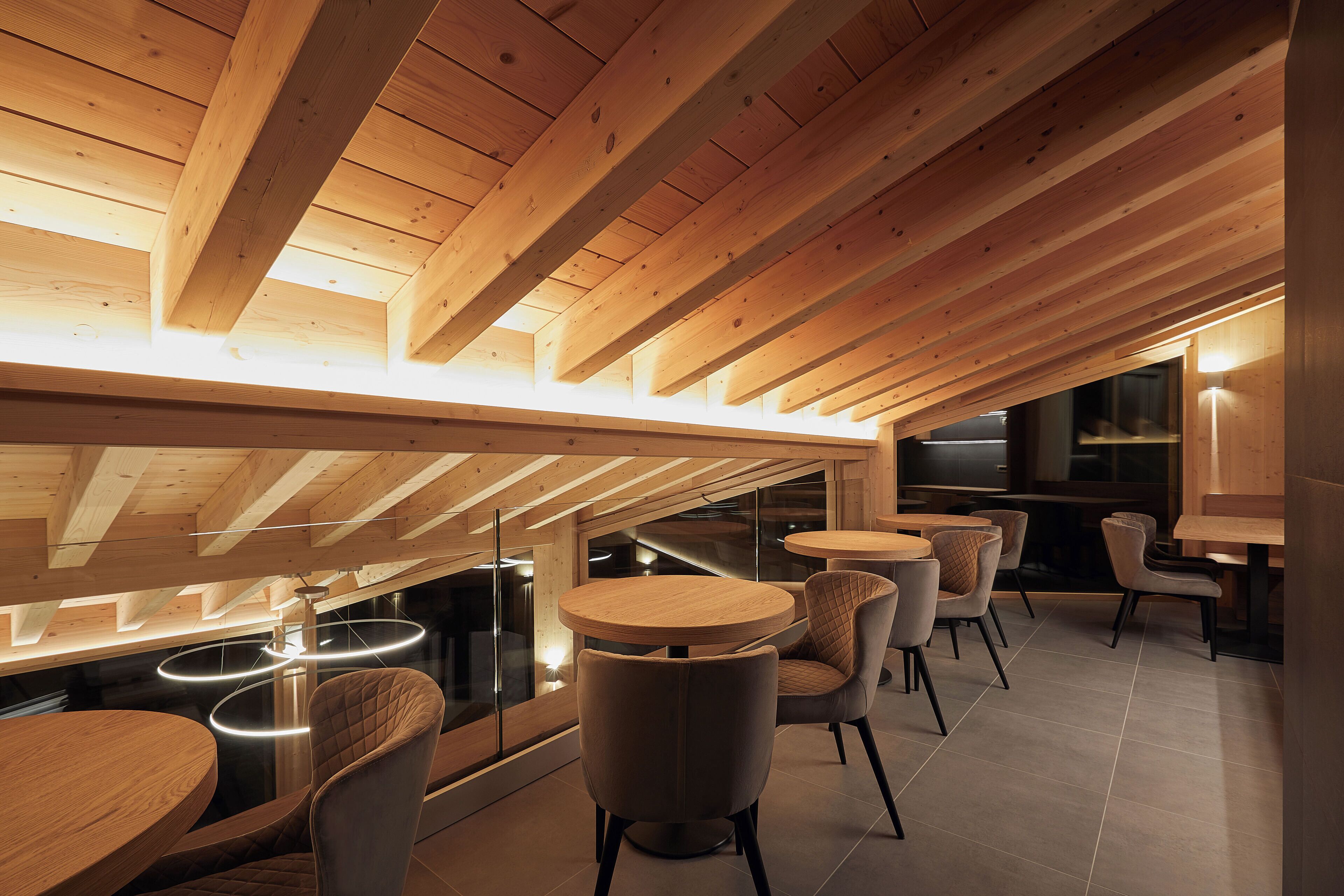 A modern interior with wooden beams, round tables, and cushioned chairs.