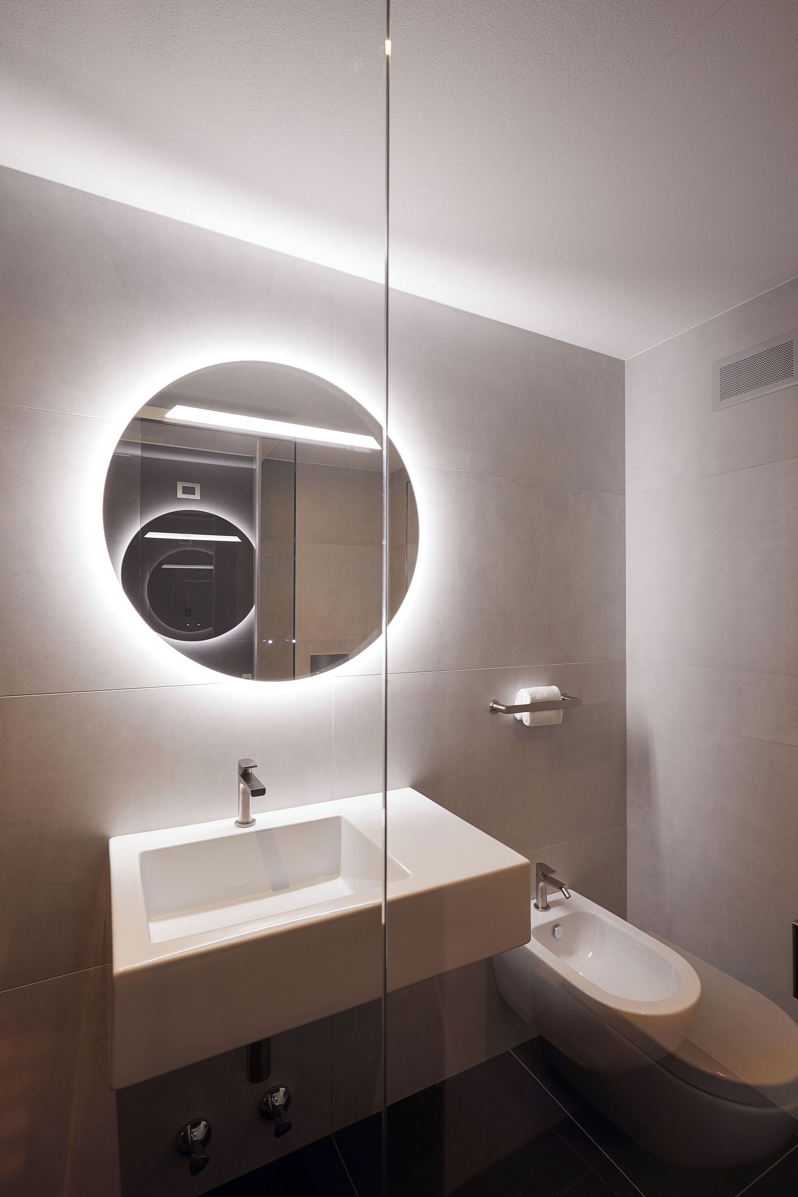 Un baño moderno con un espejo redondo, un lavamanos y un bidé.