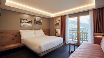 Une chambre d’hôtel moderne avec un grand lit, une petite table et un balcon offrant une vue sur les montagnes.