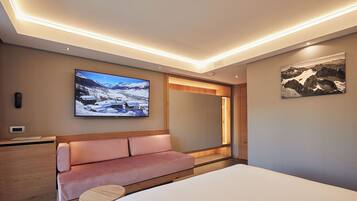 Una habitación de hotel moderna con una cama, un sofá, una mesita, un televisor y un cuadro en la pared.