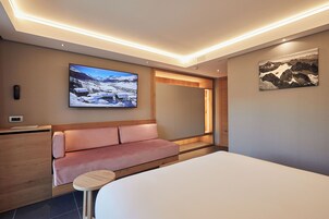 Una habitación de hotel moderna con una cama, un sofá, una mesita, un televisor y un cuadro en la pared.