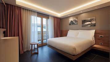 Una habitación de hotel moderna con una cama grande, un taburete pequeño y vistas a un paisaje montañoso a través de la ventana.