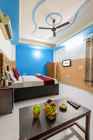 Une chambre d’hôtel avec un lit, un bureau doté d’une bouilloire, un panier de fruits et un ventilateur de plafond.