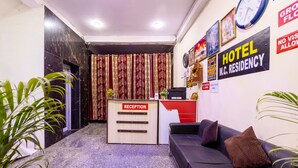 A hotel reception area with a reception desk labeled "RECEPTION," a sofa, and a clock on the wall. - Hotel M.C Residence (New Delhi)