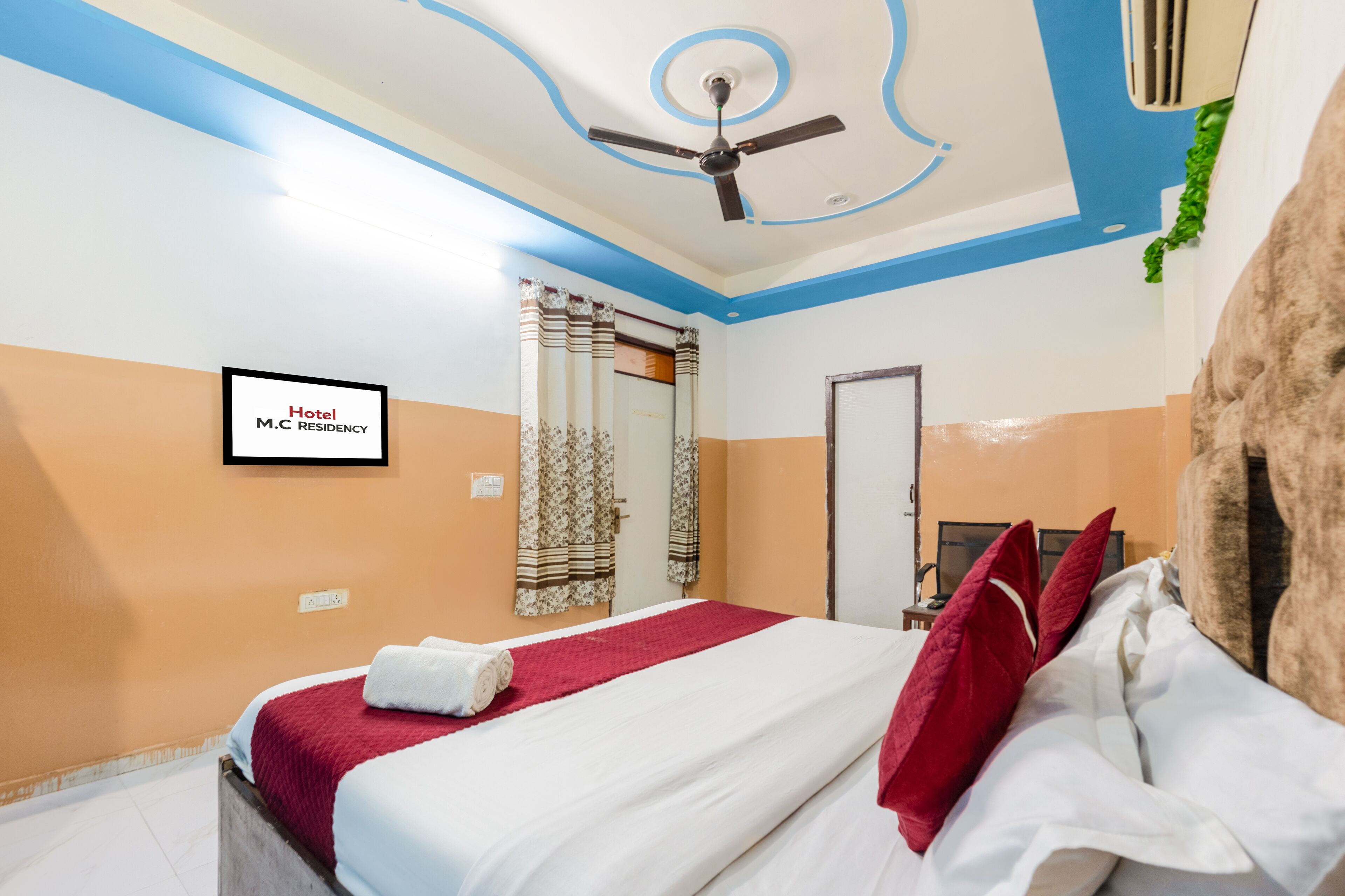 Ein Hotelzimmer mit Bett, Deckenventilator, einem gerahmten Schild an der Wand und einer Tür.