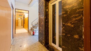 A hallway with a marble floor, a staircase, and a door with a glass panel. - Hotel M.C Residence (New Delhi)