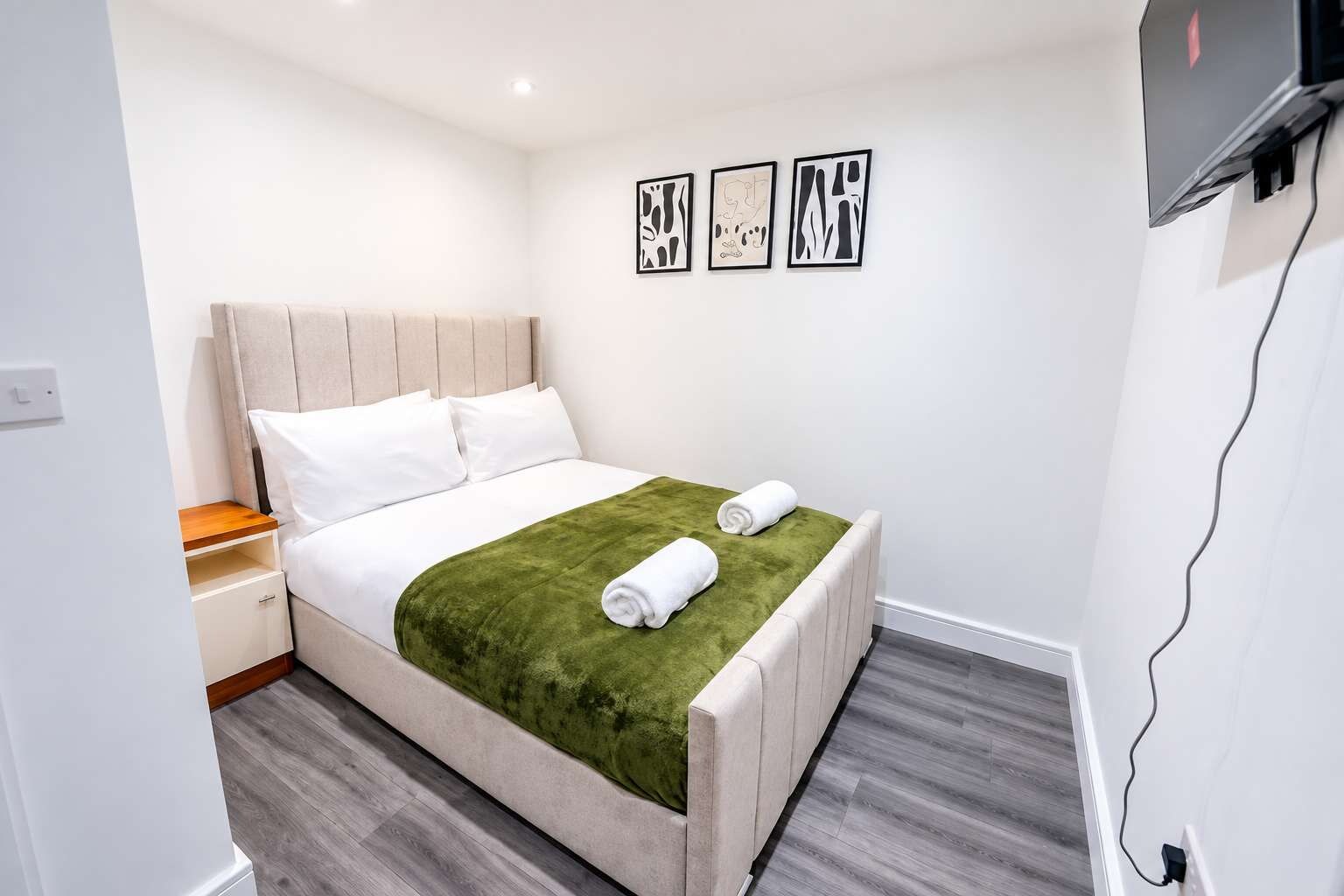 Ein Hotelzimmer mit einem Bett, einem Nachttisch, einer grünen Tagesdecke und drei gerahmten Kunstwerken an der Wand.