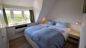 Ein Schlafzimmer mit einem Bett, einem Fenster mit Vorhängen, einem Nachttisch und einer Wandleuchte.