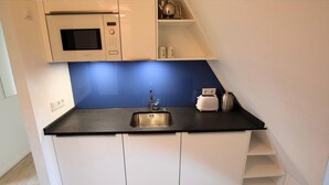 Eine kleine Küche mit Mikrowelle, Toaster und Wasserkocher auf der Arbeitsfläche, einem Spülbecken und weißen Schränken.