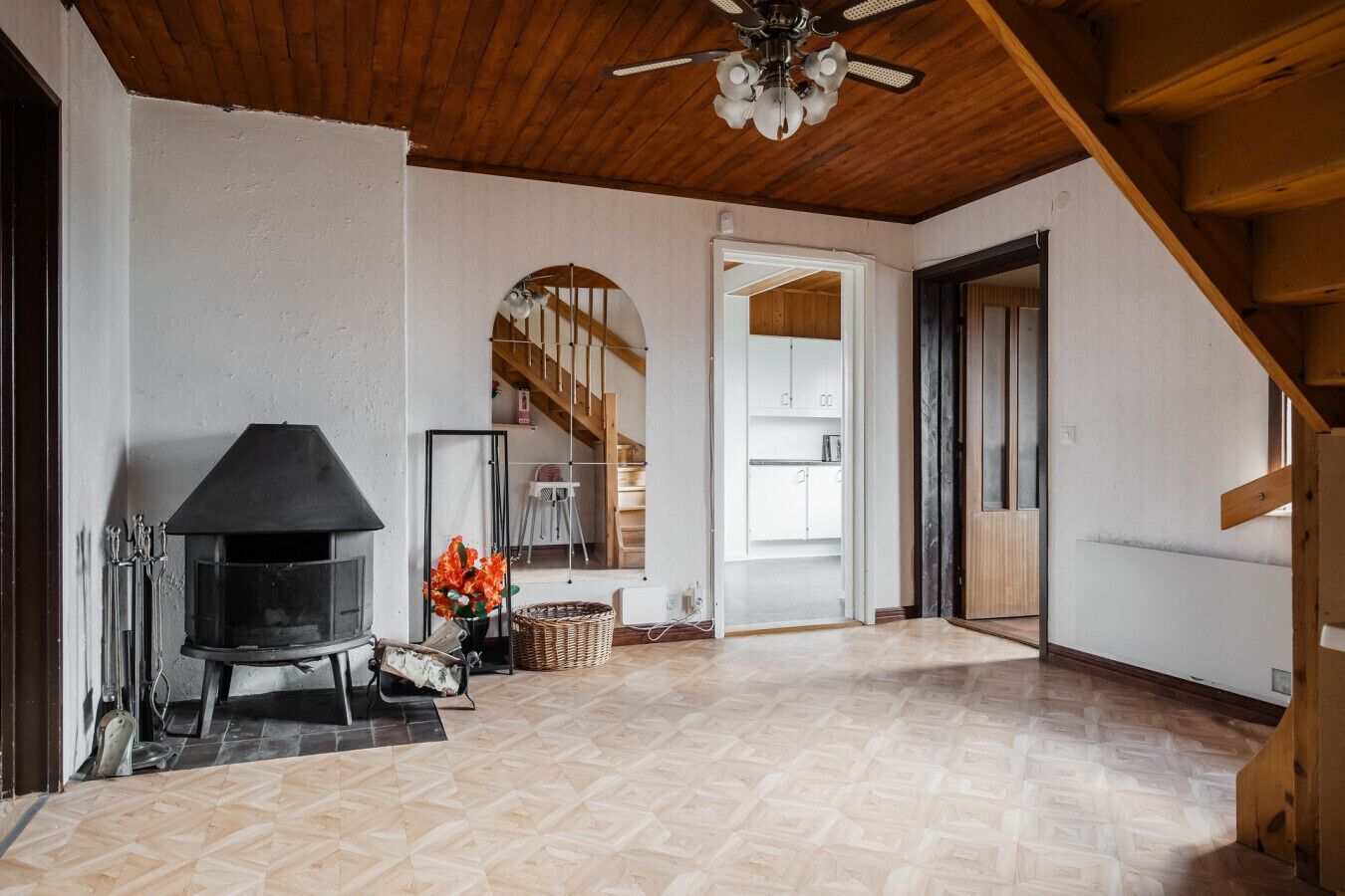 Een ruime kamer met een open haard, een houten plafond en een trap naar een ander niveau.