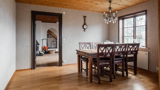 A dining area with a wooden table and chairs, a chandelier, and a clock on the wall. - Cozy Country Home in Quiet Töreboda (Töreboda)