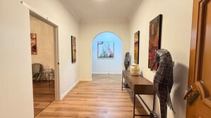 A hallway with wooden flooring, a bench, and various artworks on the walls. - Cozy family-friendly homestay in Bankstown! (Bankstown)
