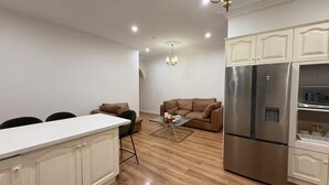A modern kitchen with white cabinetry, a stainless steel refrigerator, and a dining area with a glass coffee table. - Cozy family-friendly homestay in Bankstown! (Bankstown)