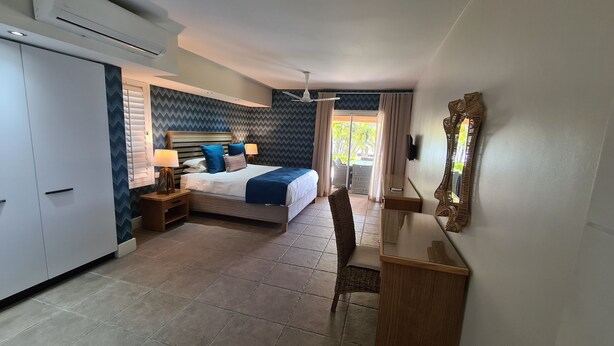 Ein Hotelzimmer mit Bett, Nachttisch, Lampe, Stuhl, Schreibtisch und einem großen Spiegel.