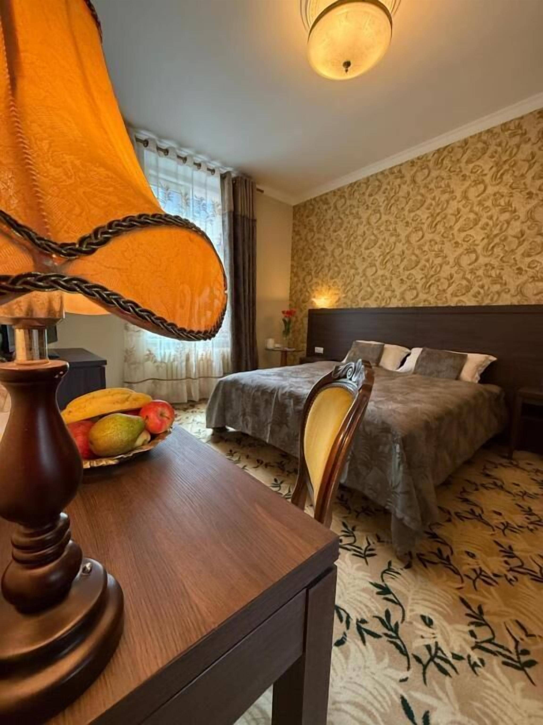 A hotel room with a bed, bedside table, lamp, and a fruit basket.