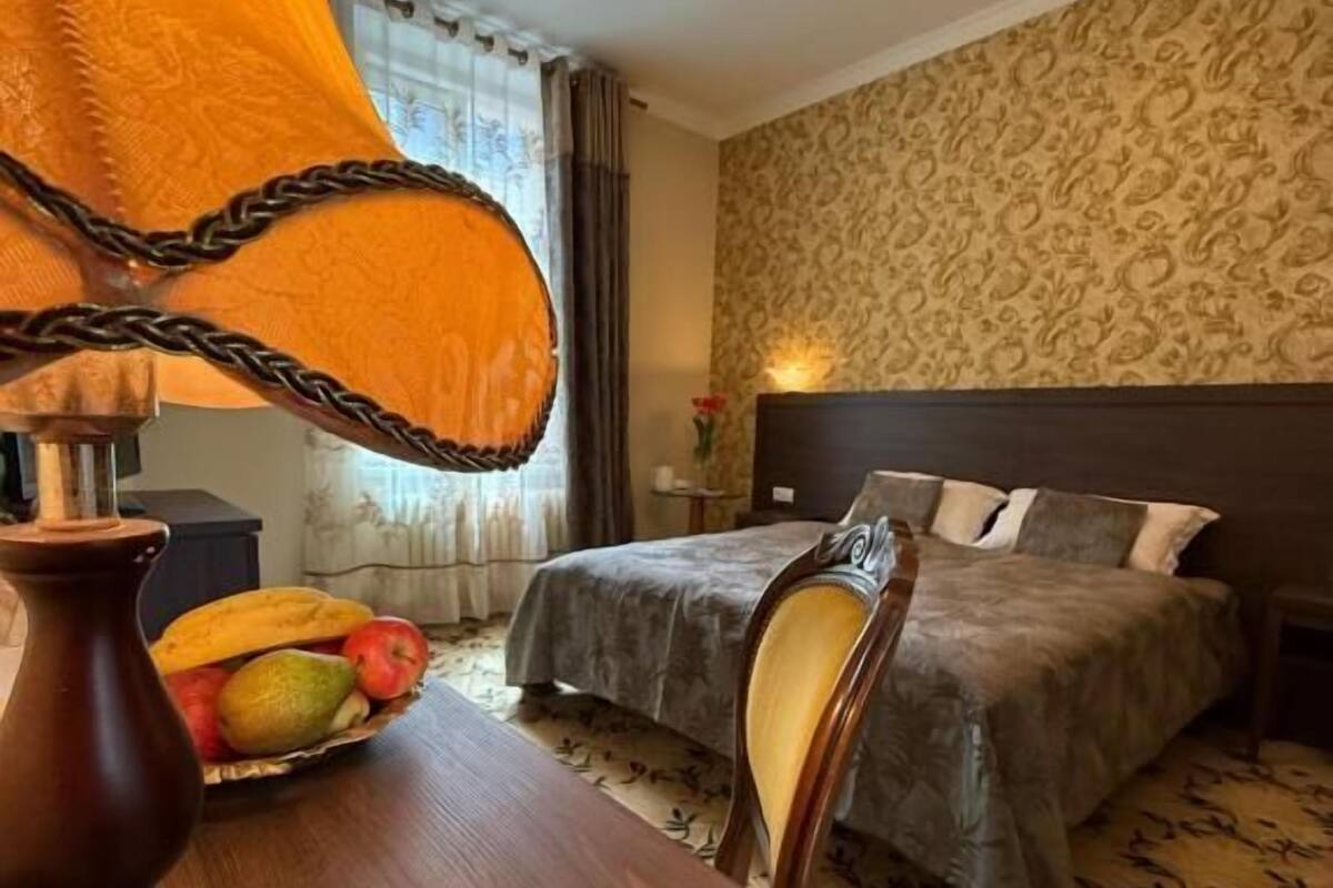 A hotel room with a bed, bedside table, lamp, and a fruit basket.