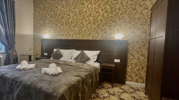 A hotel room with a large bed, a nightstand, a wardrobe, and patterned wallpaper.