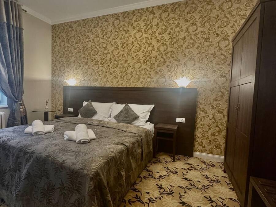 A hotel room with a large bed, a nightstand, a wardrobe, and patterned wallpaper.