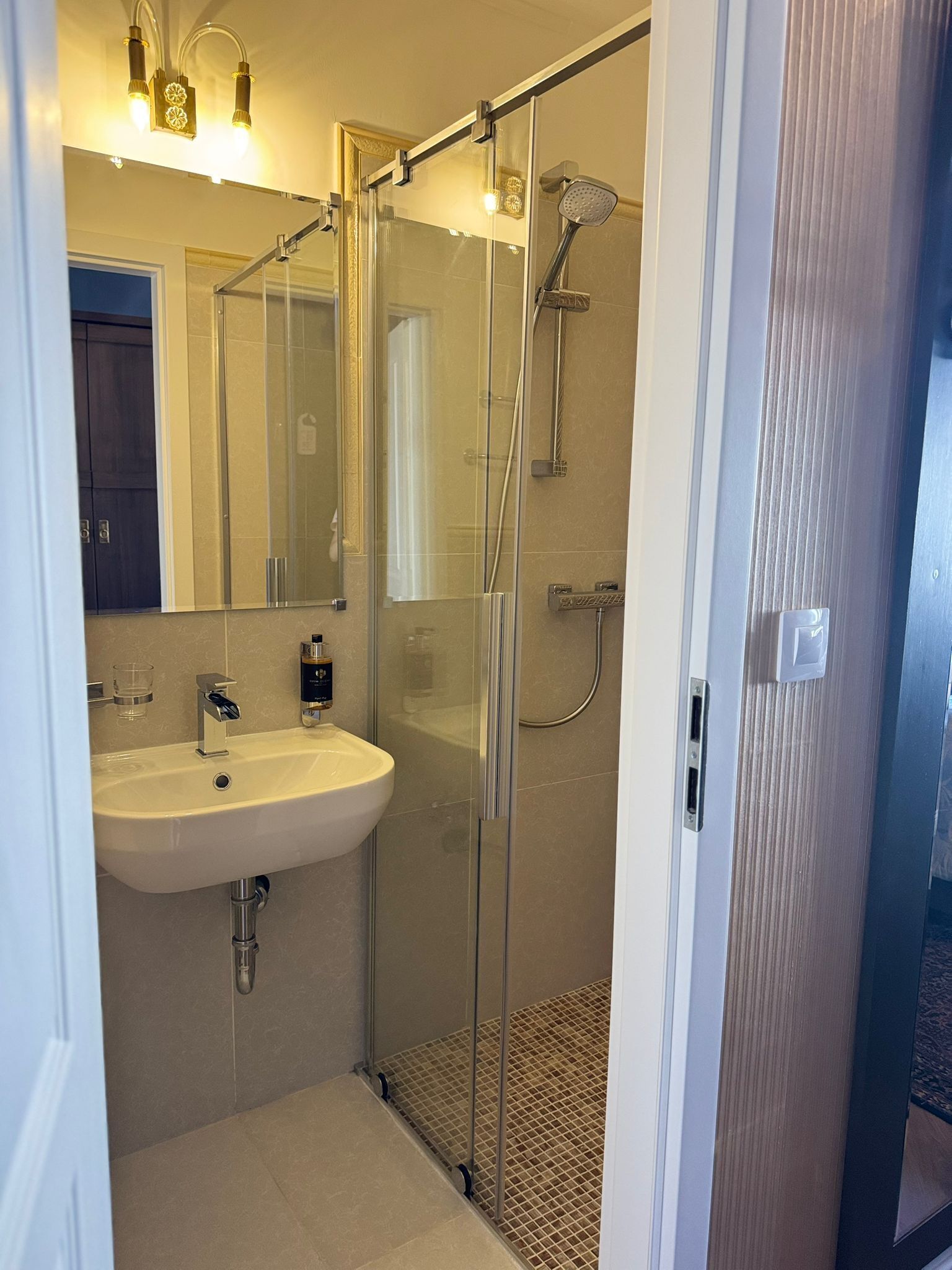 Ein modernes Badezimmer mit einer Glaskabine zur Dusche, einem weißen Waschbecken und einem Spiegel.