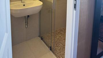 Ein modernes Badezimmer mit einer Glaskabine zur Dusche, einem weißen Waschbecken und einem Spiegel.