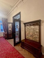 Un pasillo con alfombra roja de diseño, una puerta de madera oscura con detalles ornamentales y una obra de arte grande en la pared.