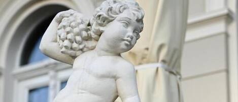 Una estatua de mármol blanco de un ángel con un racimo de uvas en la cabeza, ubicada en una barandilla.