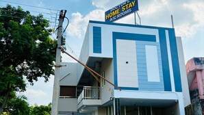 Een modern, tweelaags gebouw met een bord waarop staat: 'DOCTOR'S HOME STAY A/C ROOMS'.