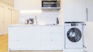 A compact kitchen with white cabinetry, a built-in microwave, a coffee maker, and a front-loading washing machine. - Lovely studio for rent (Montréal)