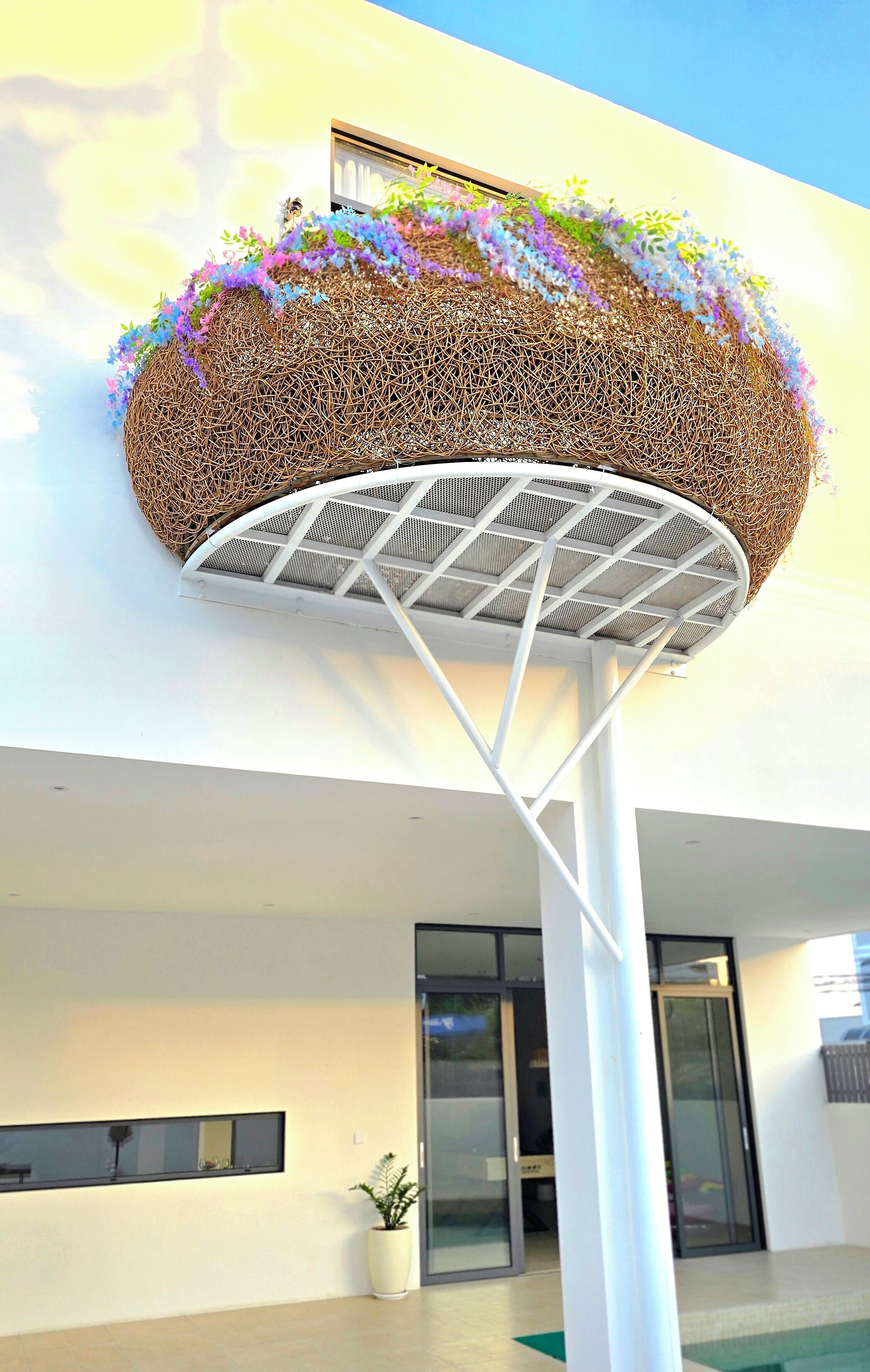 A basketball hoop with a woven basket and flowers on top, set against a modern building facade.