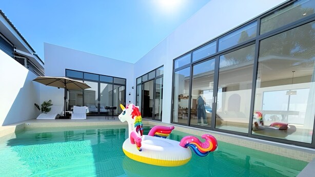 A swimming pool with a unicorn float, modern architecture, and large windows. - Quint Pool Villas (Pattaya)