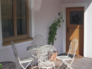 A patio with a round table and four metal chairs, a potted plant, and a wooden door. - Delightful 2-bedroom apartment in charming Hof bei Salzburg awaits you (Hof bei Salzburg)