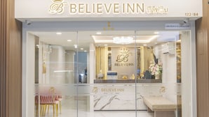 The entrance of a hotel named BELIEVE INN with a modern design, featuring a reception desk and a seating area with chairs and a bench. - Believe Inn (Bangkok)